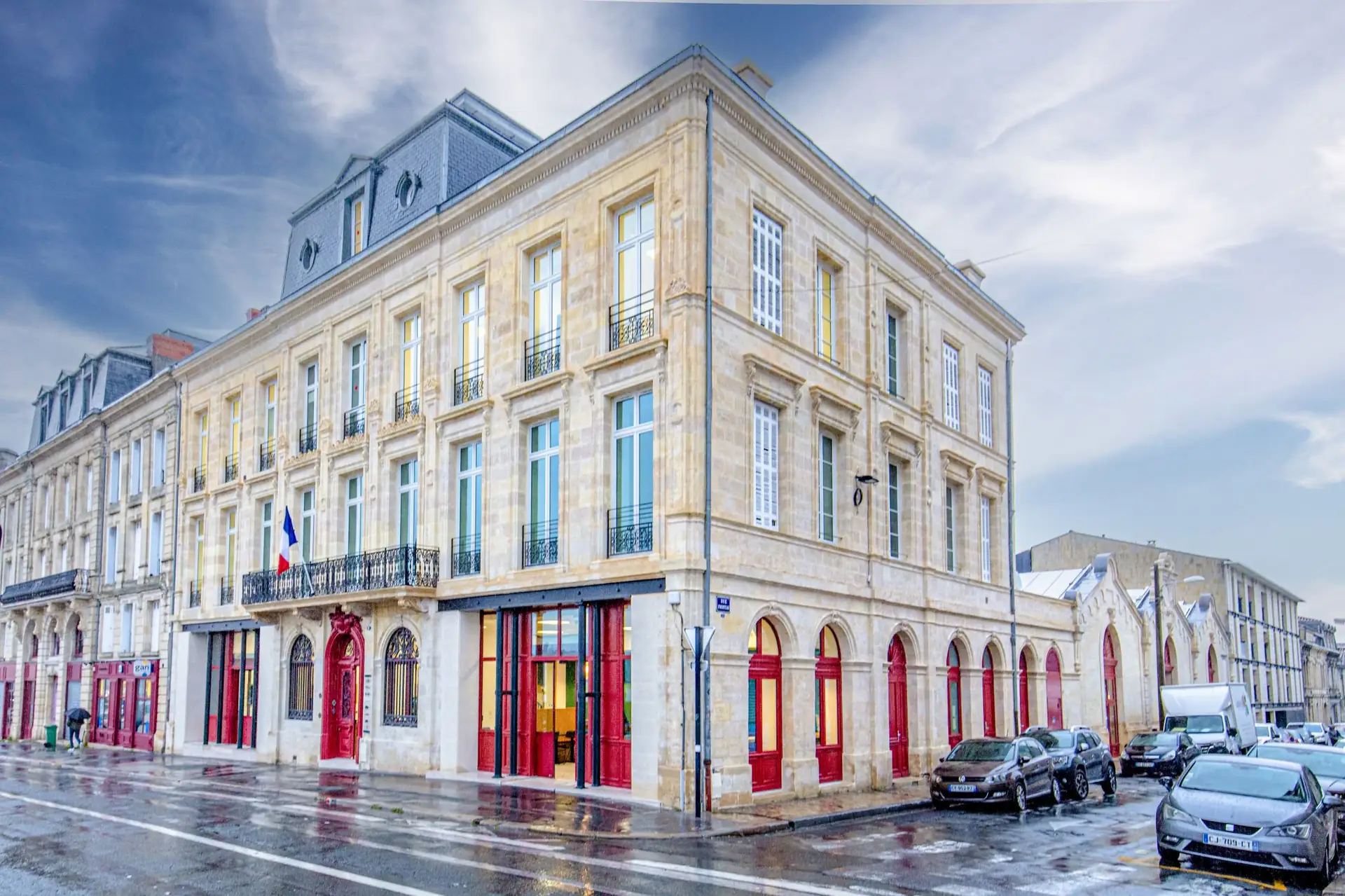 Façade en pierre blonde réhabilitée du projet Queyries à Bordeaux, menuiseries rouges en rez-de-chaussée